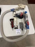 Full view of four air-powered tools on table including cutoff tool, hand sander, orbital sander, and air file board with dust collection hose and cloth bag