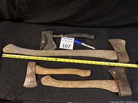 Photo shows all four axes laid out horizontally, two small to medium wood handled axes, one large wood handled axe with measuring tape for size approximate.