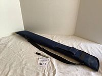 Full view of a dark blue fishing rod bag with shoulder strap laid flat on a surface.