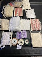 Multiple lace trims and three lace ribbon spools displayed on a black surface. Different colors and styles of lace visible.