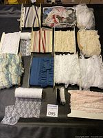Top-down image showing assortment of fabric laces arranged in rows, showcasing variety of colors, widths, lengths, and styles including floral prints and ruffles.
