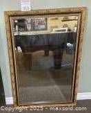 Mirror standing against a beige wall, showing full frame and reflection of surrounding furniture and artwork.