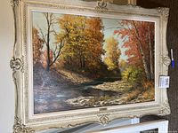 Framed oil painting of a forested autumn landscape with a creek, showing rich colors in trees and detailed brushwork.
