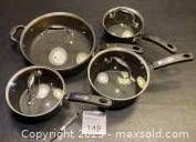 Set of five black non-stick pots and pans, all with handles, arranged on a black surface with lids on four of the pots.
