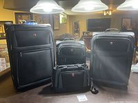Four piece set of black SwissGear luggage in a room with overhead lighting.