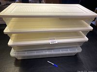 Four shallow rectangular storage totes stacked with three opaque Rubbermaid totes and one clear plastic tote at the bottom. Two totes have an inner tray.