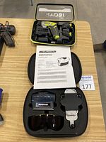 Overview of Ryobi cordless screwdriver with charger and changeable heads in case, Mastercraft laser level set with case, laser glasses, and instruction manual on table.
