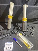 Two PRIME fluorescent trouble lights, one with two hooks, one with one hook broken. Includes an unopened spare replacement bulb and a marker for scale.