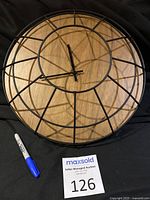 Front view of round wood wall clock with black metal cage frame and visible clock hands on wooden face.
