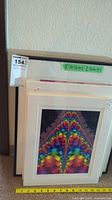 Several stacked framed and unframed artwork pieces showing size labels and edges of the frames.