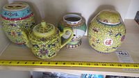 Photo of all four Asian themed ceramic items including teapot and vases on shelf with measuring tape