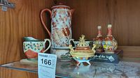 Shelf display featuring various Asian themed ceramic items including teapot, creamers, vases, and incense burner.