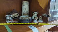 Full view of the lot inside a wooden cabinet shelf showing the ceramic items, including plates, vases, and shaker set