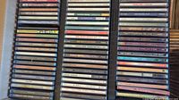 Photo showing multiple stacks of CDs featuring a variety of artists and titles in jewel cases.