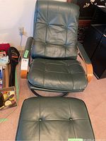 Front view of a semi-reclining armchair with dark green faux leather, wooden armrests and metal base, alongside matching ottoman.