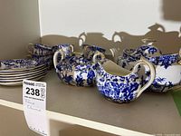 Photo showing the full set of bone china tea items: six tea cups, six saucers, teapot, cream jug, and sugar bowl in blue and white with gold trim.