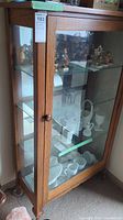 Front view of the display cabinet showing wood frame, glass doors and interior glass shelves with mirror back.