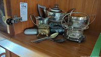 Full view of silverware set including teapot, jug, creamer, spoons and other pieces on wooden shelf