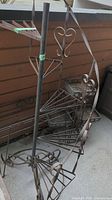 Tall spiral metal plant stand showing three triangular shelf platforms and decorative heart-shaped accents on the frame