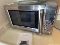 Front and side view of the Breville Quick Touch microwave oven showing stainless steel body, door handle, and control panel with digital display.