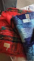 Two mohair blankets folded, one mostly red/orange and another in blue tones.