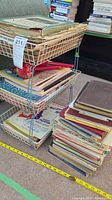 Stacked wire racks and piles of assorted vintage sheet music and songbooks on carpeted floor