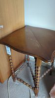 Side view of vintage wooden folding side table showing turned bead legs and cross stretcher, note wear and damage marks on wood tabletop.