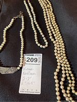 Four vintage pearl necklaces laid flat on black surface with measurement note and MaxSold tag.
