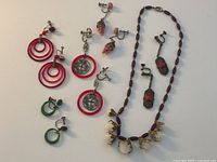 Overview of the lot showing six pairs of clip-on earrings in various colors and designs and one beaded necklace with carved rose accents.