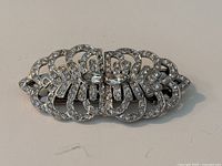 Front view of the 1930s silver-tone rhinestone duette brooch, showing its detailed openwork design with clear rhinestones and two central large rhinestones.