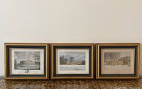 Three framed prints displayed side by side on woven surface against white wall