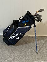 Side profile of Callaway golf bag with clubs and visible collapsible legs with plastic wrap.