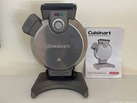 Front view of Cuisinart vertical waffle maker showing stainless steel round body with Cuisinart logo, browning control dial, indicator lights, and locking handle.