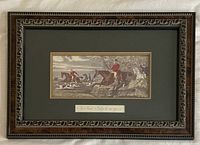 Photo of the framed fox hunt print showing the scene of riders and hounds, with visible decorative wooden frame and matting including inscription label.