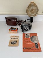 Full lot arranged with Kodak Retina IIa camera, leather case, flash unit, box of flash cubes, and manuals.
