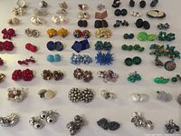 Wide view of the lot showing a variety of vintage clip on and screw back earrings in multiple colors and styles arranged on a flat surface.