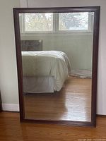 Full view of the rectangular vintage mirror leaning against a wall with a bed and window reflected in the glass.