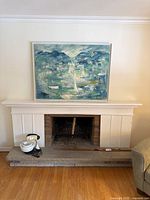 Framed vintage canvas artwork depicting abstract coastal harbor scene with mountains and boats placed above fireplace mantel.