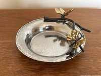 Top-side angle view of twisted branch and ginkgo leaves detail on silver dish coaster.