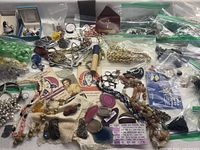 Wide view of assorted vintage and pre-owned jewelry pieces laid out including beaded necklaces, metal chains, brooches, and vintage ephemera.