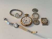 Six watches arranged on table including pocket watch, wristwatches, mesh and expansion bands