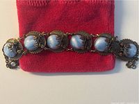 Full view of the bracelet showing six large round blue cabochon stones set in decorative filigree metal frames with an adjustable chain clasp.