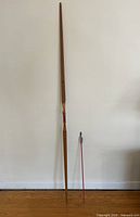 Full length view of bow and one arrow standing upright against wall showing size and shape