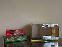 Front and side view of the yellow Lincoln vintage metal bread box with chrome front, accompanied by boxed Miracle French Fry cutter and Magic dusting paper products on a reflective surface