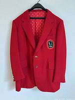 Full front view of the bright red blazer jacket with flap pockets and embroidered crest patch on chest pocket.