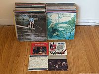 Photo showing stacks of over 80 vintage vinyl records including a Joni Mitchell album on the front and 4 singles displayed in front.