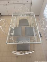 Overhead view of rectangular glass tabletop showing scrollwork frame and four chairs around.