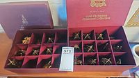 Open box showing multiple gold-tone Christmas ornaments neatly stored in velvet compartments inside a maroon Danbury Mint Gold Christmas Ornament Collection box.