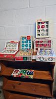 Photo of multiple boxes of vintage Shiny Brite ornaments in original boxes with various colors and styles visible on a dresser.