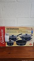 Front view of Sunbeam Newbrook black non-stick steel cookware set in unopened retail box